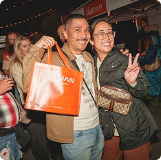 Two Food Bowl attendees smiling and showing off their event tote bag